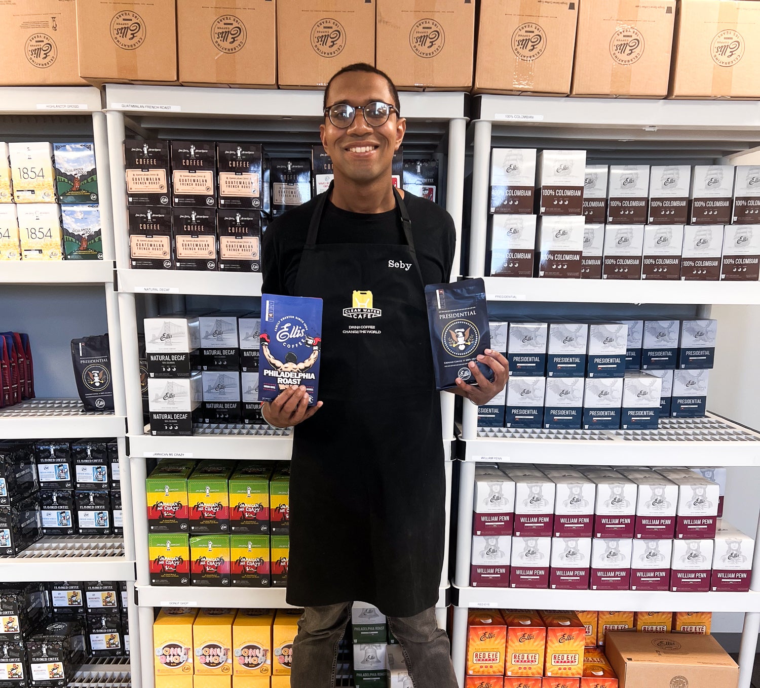 Person holding coffee packages in a store with shelves of coffee boxes.